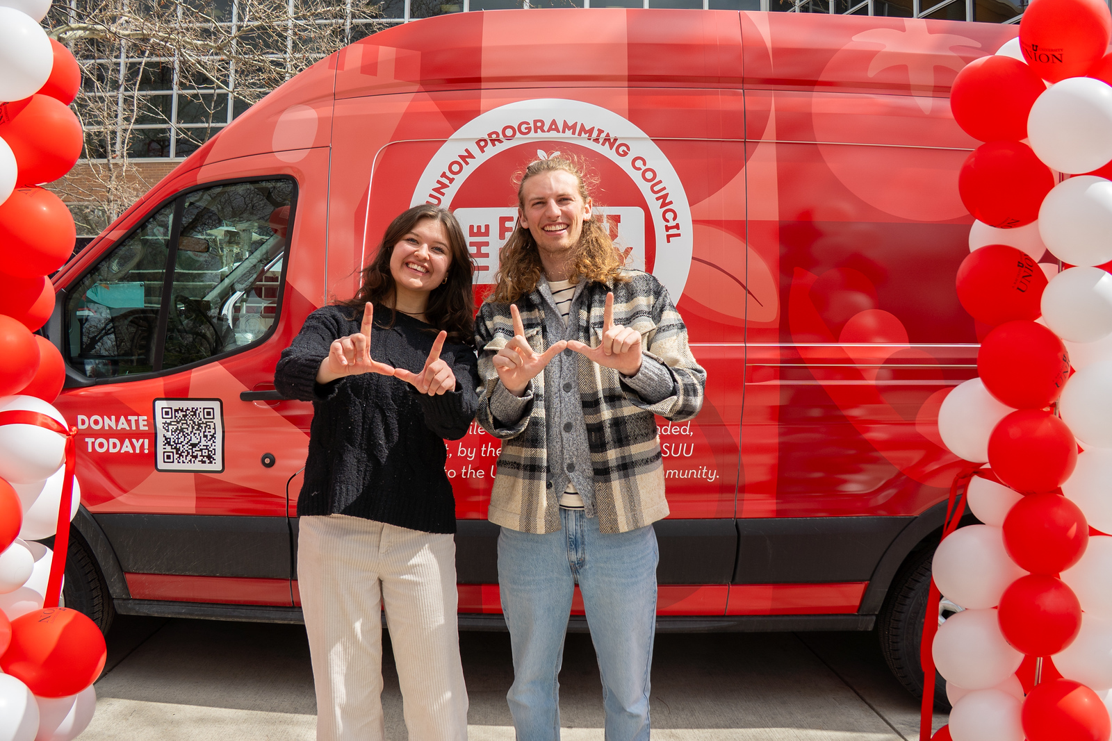 a smiling woman and a smiling man stand in front a red Feed U pantry van with U block hands